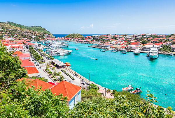 Bright and colorful harbor image of Saint Barthelemy. Aerial view with blue sky and turquoise colored water in the marina.Buildings with red roofs along the waterfront.
