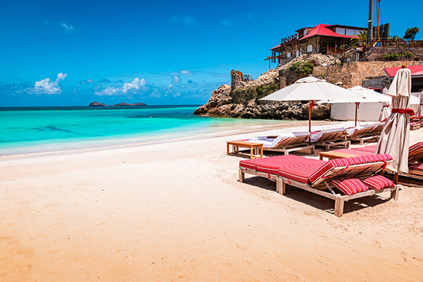 Idyllic white sandy beach, turquoise calm sea and blue sky. Luxury beach chairs with umbrella on the side of the image. Colorful landscape of St Jean beach in Saint Barthelemy, St Barts.