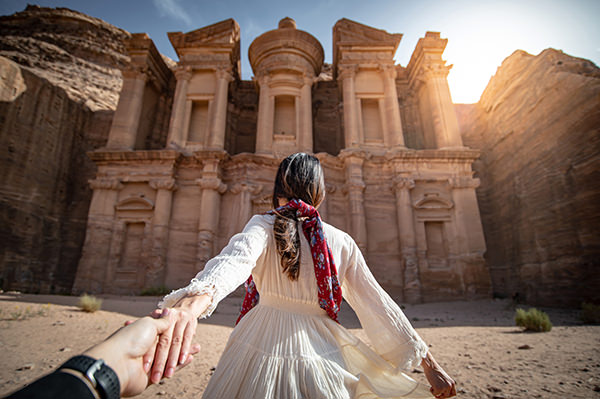 Turista de mulher asiática em vestido branco, segurando a mão de casal em Ad Deir ou El Deir, o monumento esculpido na rocha na antiga cidade de Petra, na Jordânia. Viaje pelo Patrimônio Mundial da UNESCO no Oriente Médio