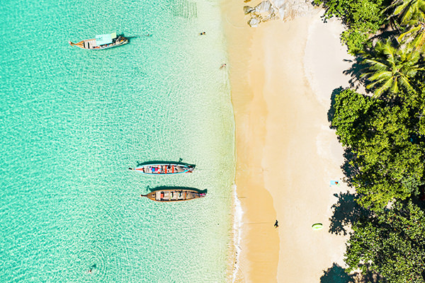 View from above, stunning aerial view of a beautiful tropical beach with white sand and turquoise clear water, longtail boats and people sunbathing, Banana beach, Phuket, Thailand.