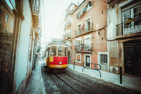 A wide-angle view of a red retro tram on a narrow street with one-way rail traffic in a European city; a vintage tourist streetcar in yellow and red colors on a tramway track over paving stone