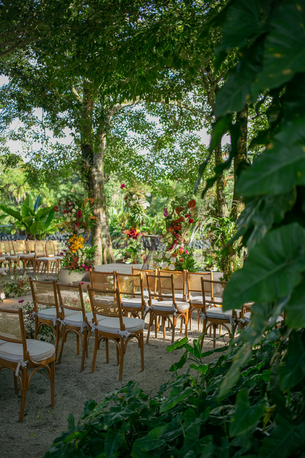 Casamento de Camilla de Lucas e Mateus Ricardo no Rio de Janeiro, espaço de acomodação para os convidados ao ar livre. Com muitas flores e folhas, as cadeiras são de madeira com assento branco 