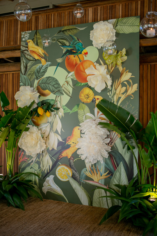 Casamento de Camilla de Lucas e Mateus Ricardo, decoração tropical com quadro de flores, quadro de flores e frutas, decoração com plantas e fundo de madeira