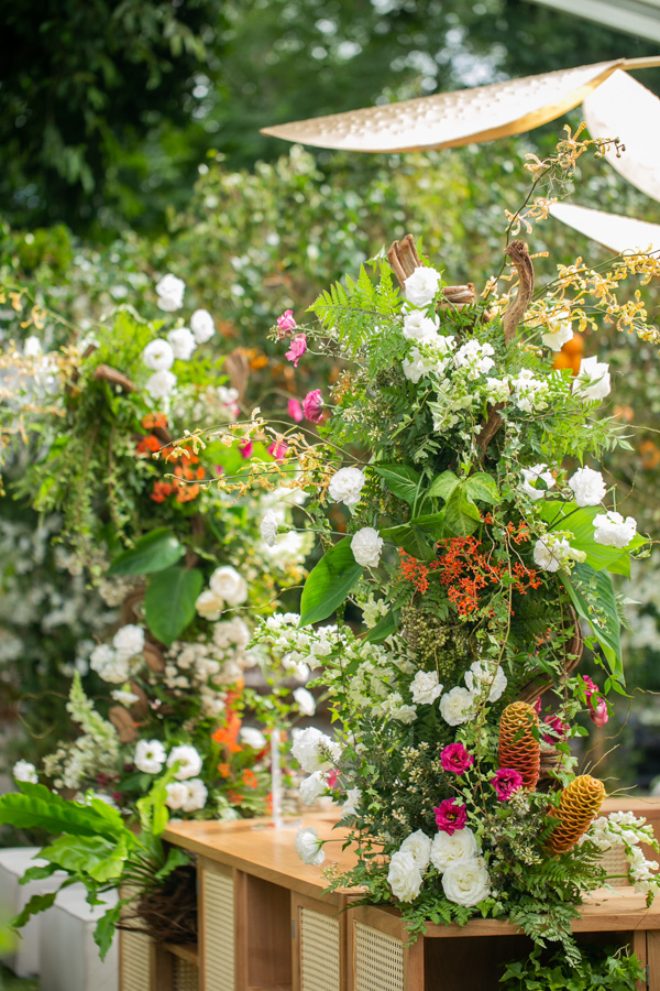 Casamento de Camilla de Lucas e Mateus Ricardo, decoração com destaue para as flores em cima da mesa do serviço de bar, mesa de madeira clara com flores brancas, rosas e laranjas em cima da mesa