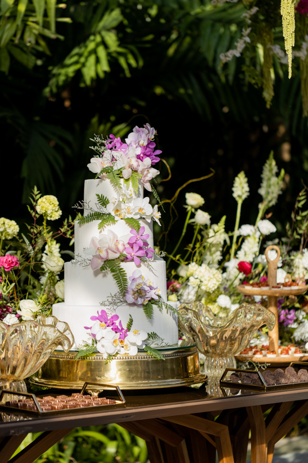mesa do bolo e de doces do casamento de Camilla de Lucas e Mateus Ricardo, bolo branco, com doces de chocolate ao lado, bolo com detalhes florais rosa claro e escuro com algumas flores brancas