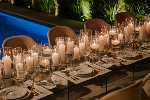 Decoração do noivado de Paula Aziz e Francisco Garcia, decoração da mesa com muitas velas tradicionais, fundo verde de folhas e azul claro da piscina 